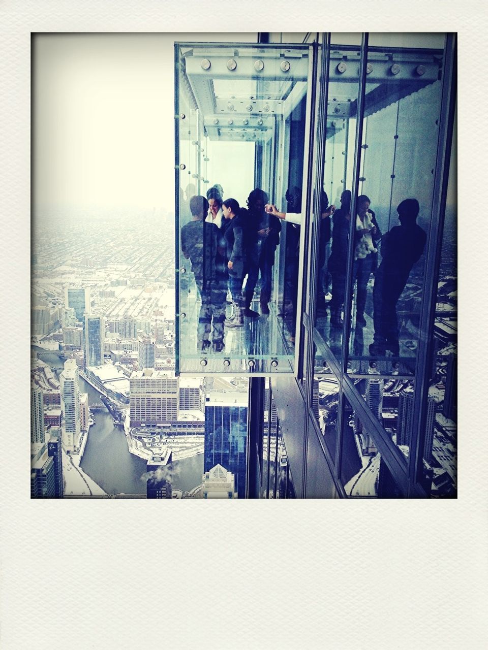 People looking at cityscape on glass ledge of building in city