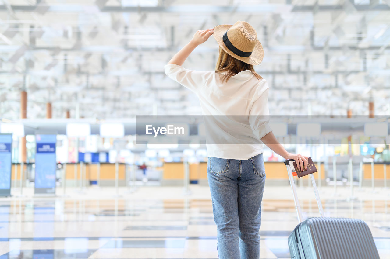 Rear view of woman wearing hat with suitcase walking at airport