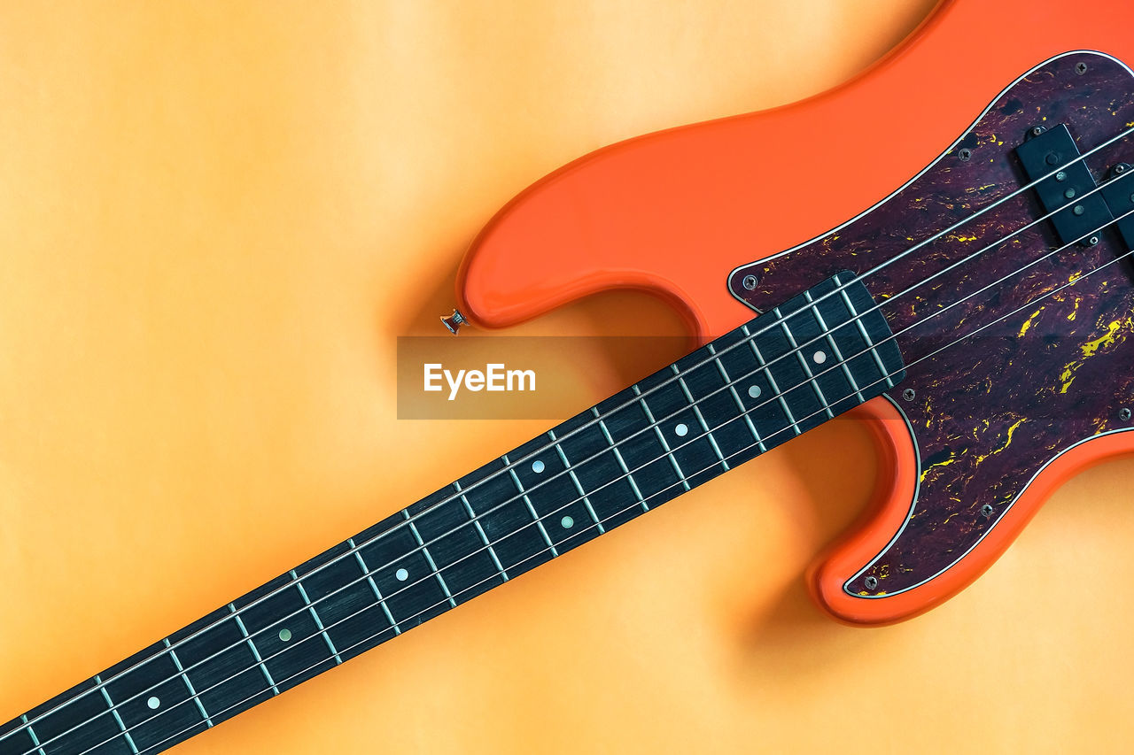 Orange electric bass guitar on orange background with copy space