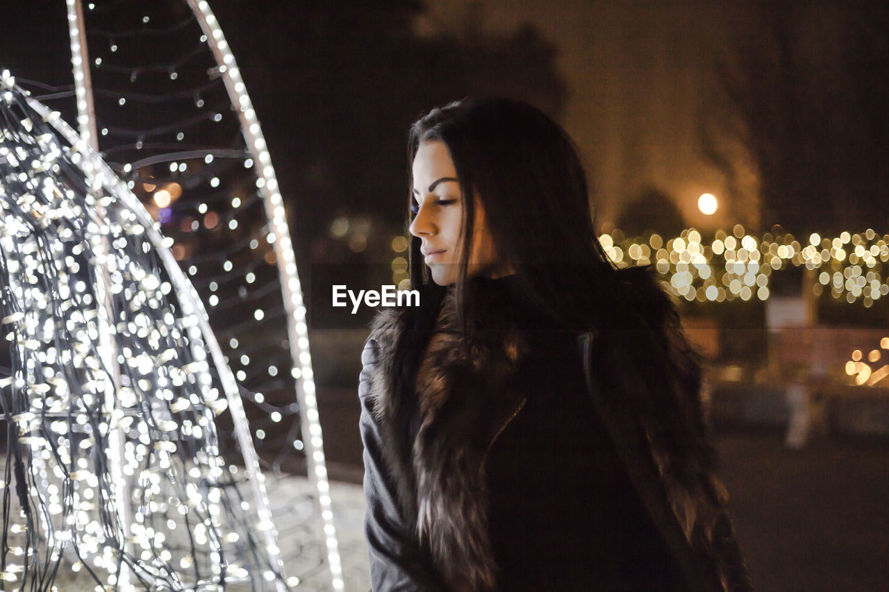 Woman with eyes closed standing by fountain at night