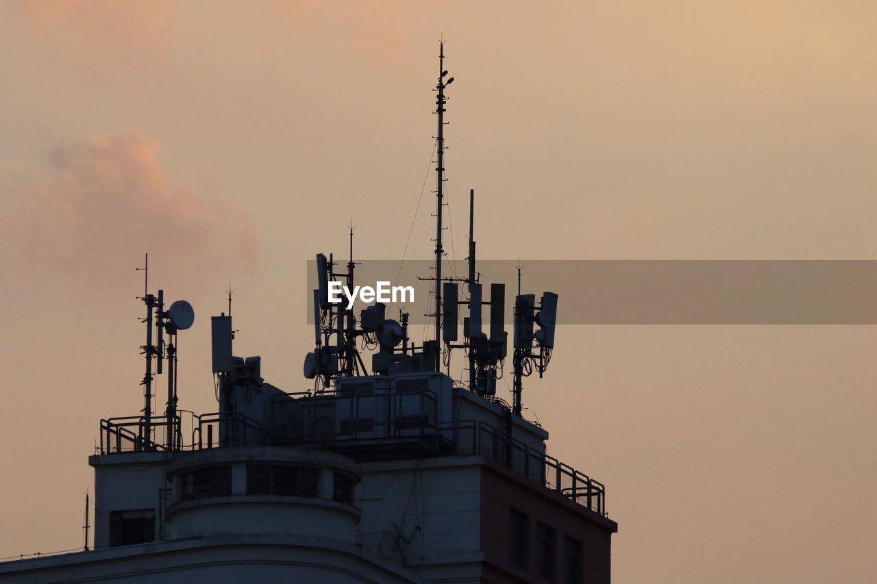 Low angle view of antennas on building against sky during sunset