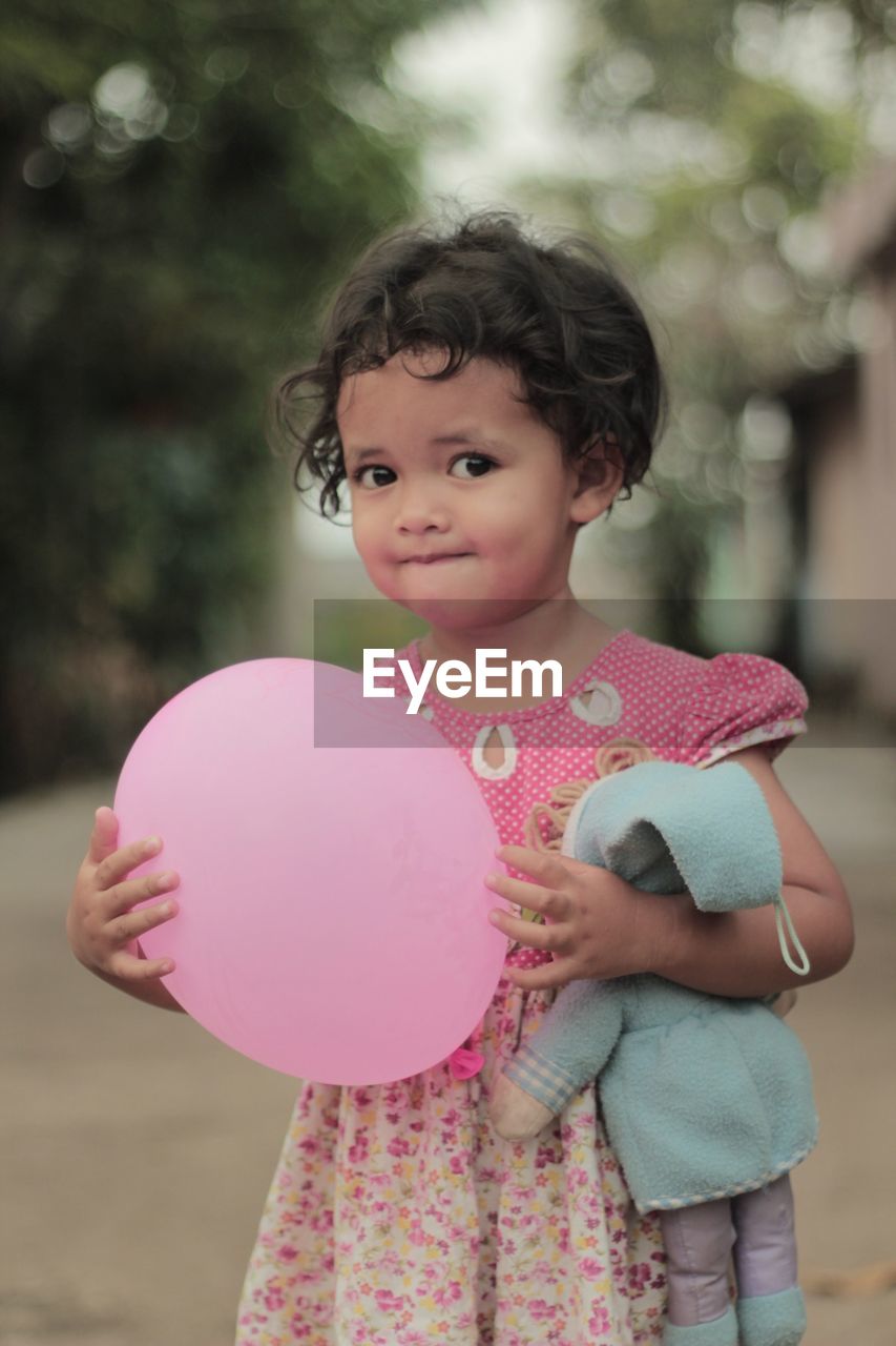 Portrait of cute girl holding balloon while standing outdoors