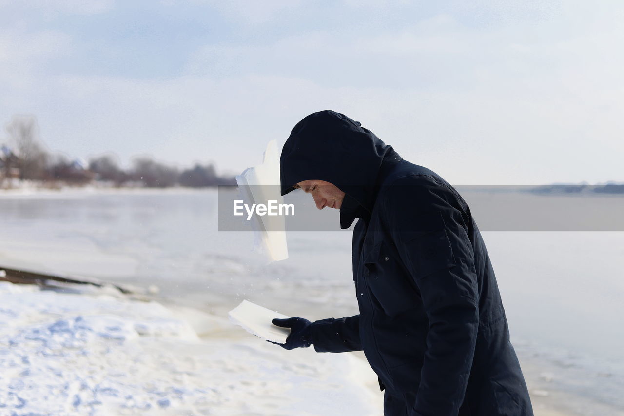 Side view of man breaking ice with head at lakeshore