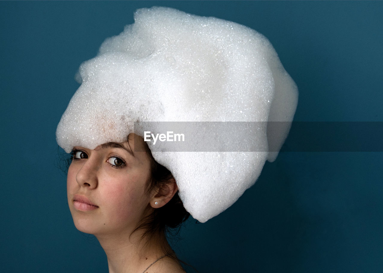 Portrait of young woman wearing hat standing against blue background