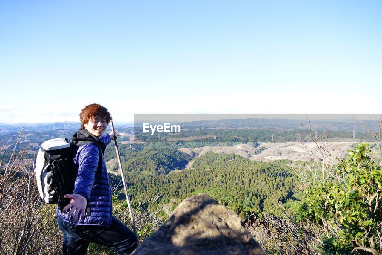 MAN STANDING ON MOUNTAIN LOOKING AT VIEW OF MOUNTAINS