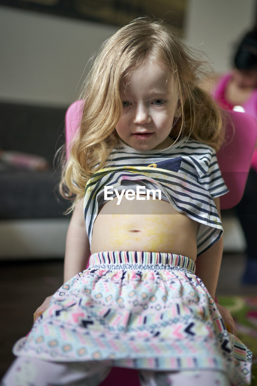 Cute little girl artist sitting on chair showing her pained belly.