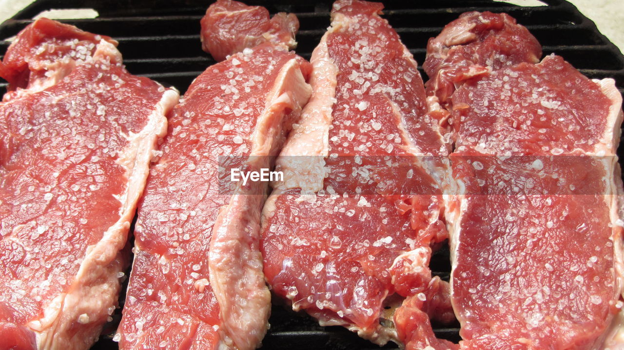 High angle view of meat on metal grate at barbecue