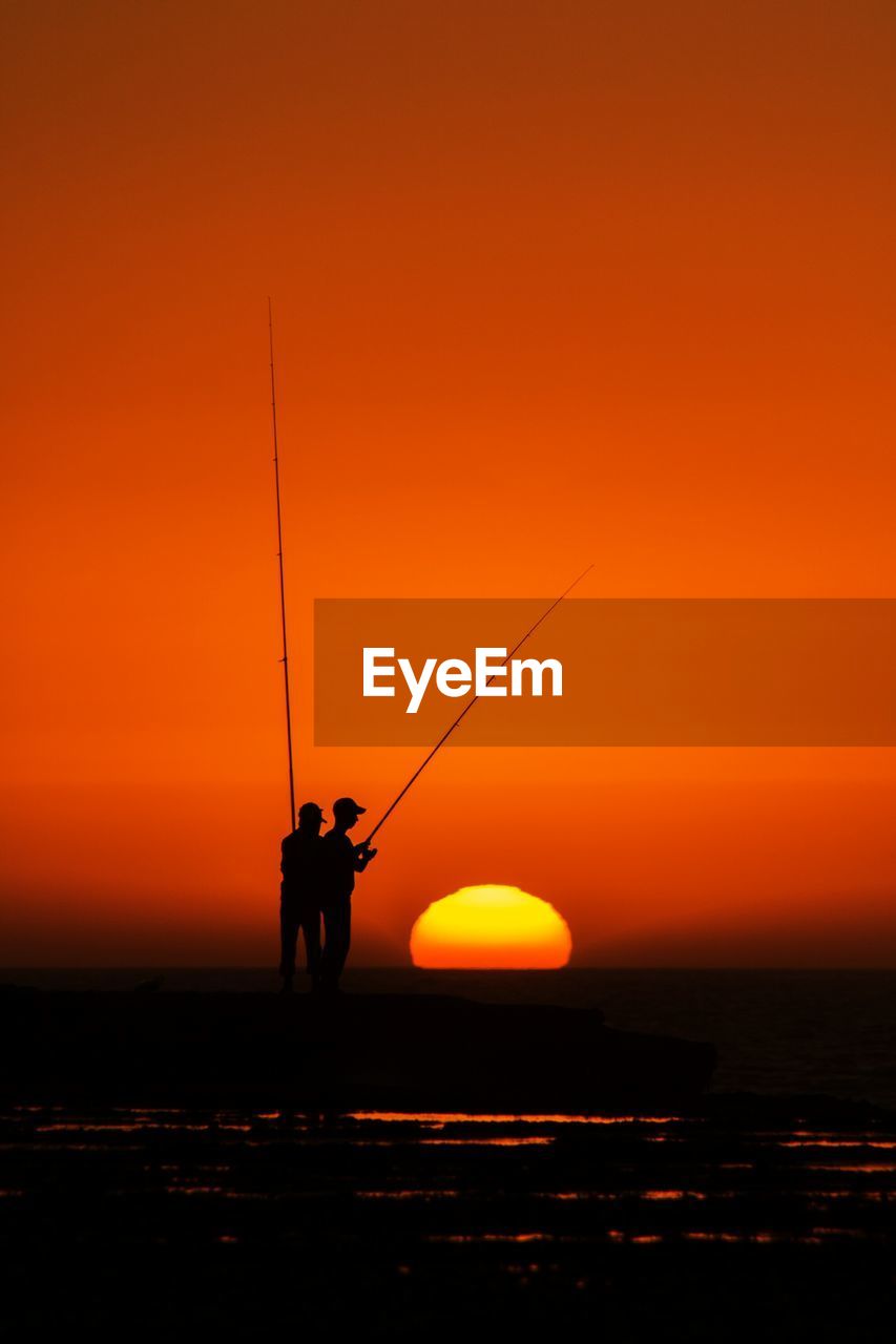 Silhouette fishermen fishing during sunset