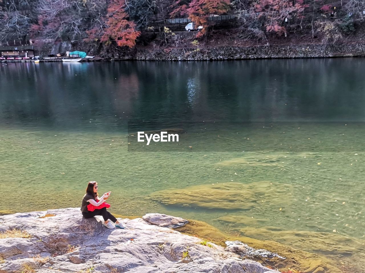 Full length of woman sitting on rock by lake during sunny day