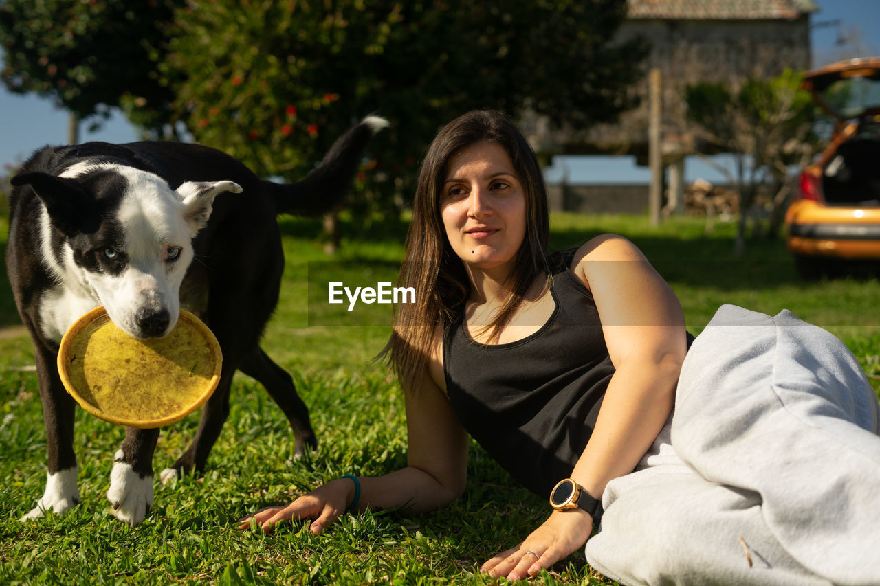 Woman lying on grass while dog standing by side