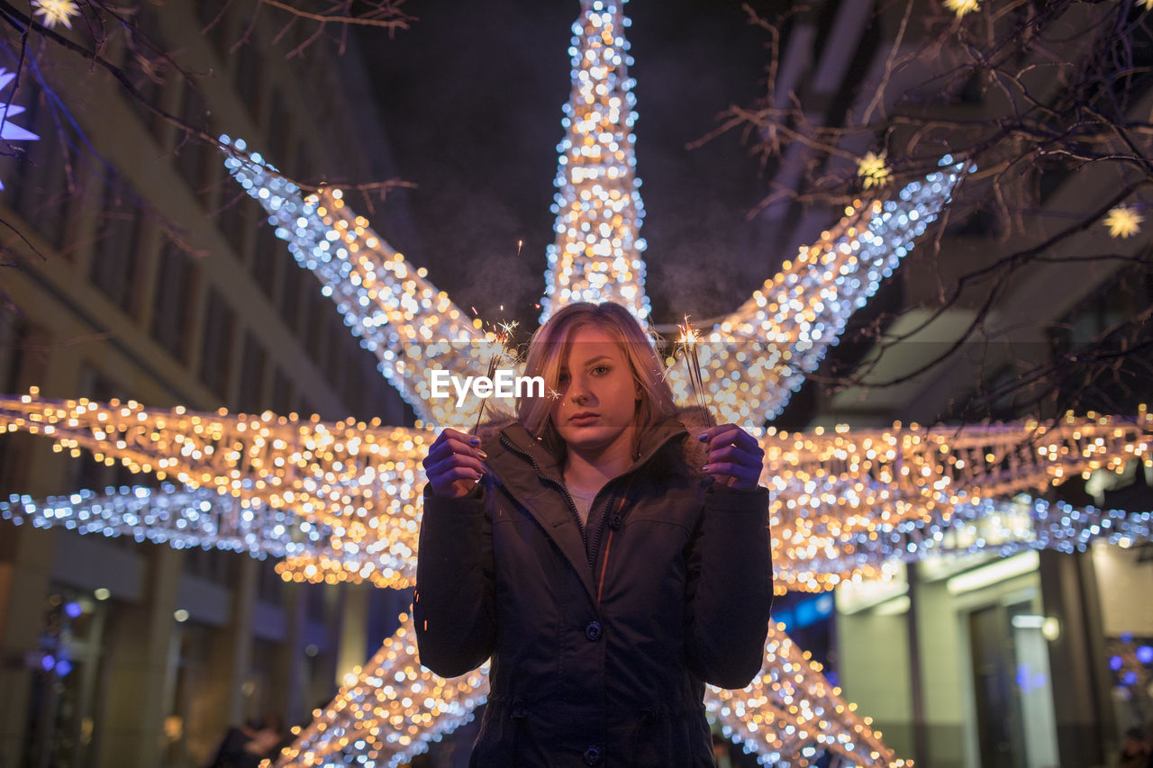 Portrait of woman holding illuminated sparkler at night