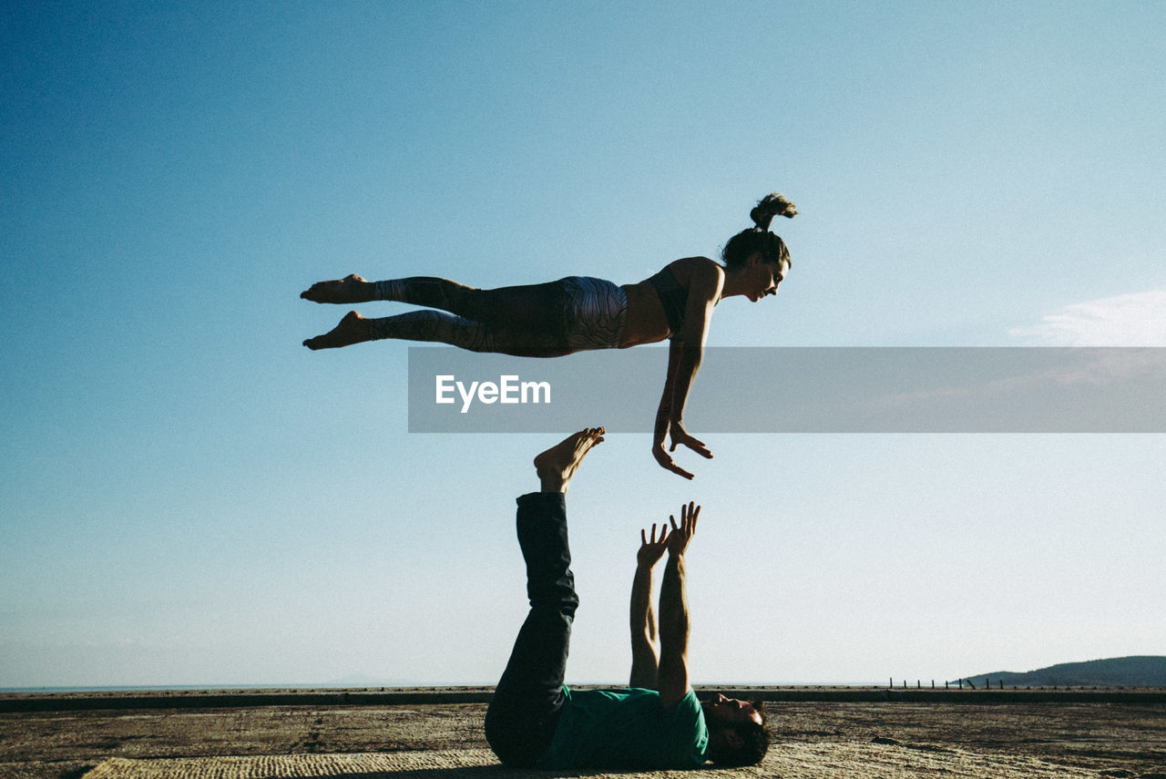 Full length of man balancing woman against clear sky