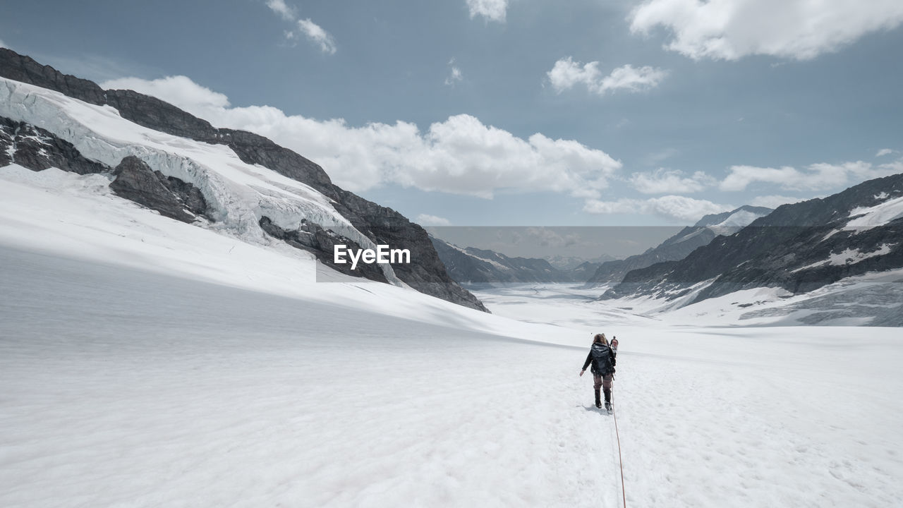 REAR VIEW OF MAN ON SNOWCAPPED MOUNTAIN