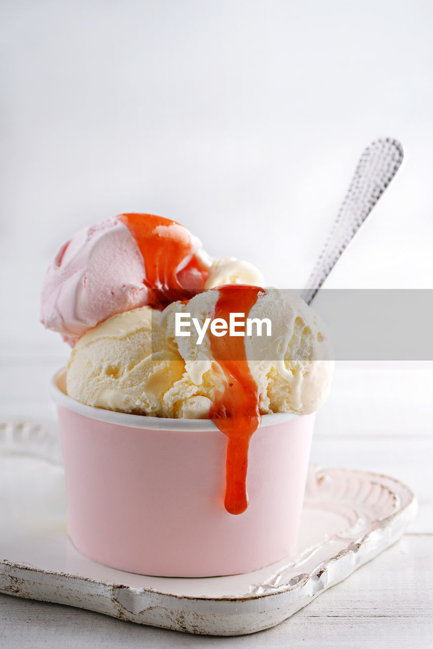 Ice cream in pink cup with spoon on tray against white background