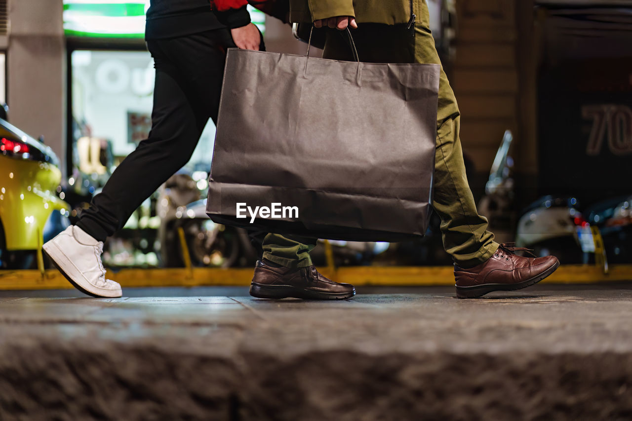 Two people walking through the city at night, one carrying a large shopping bag.