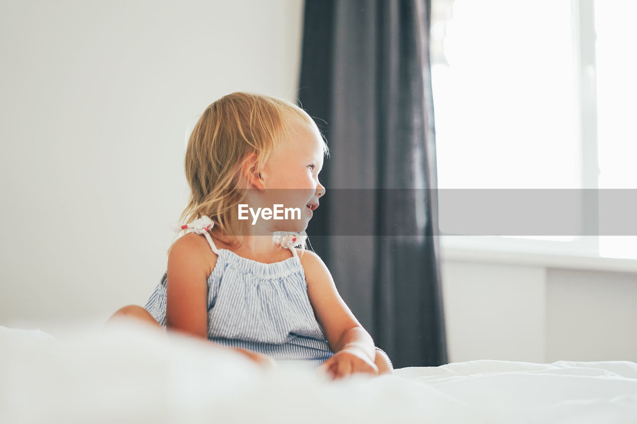 Girl looking away while sitting on bed