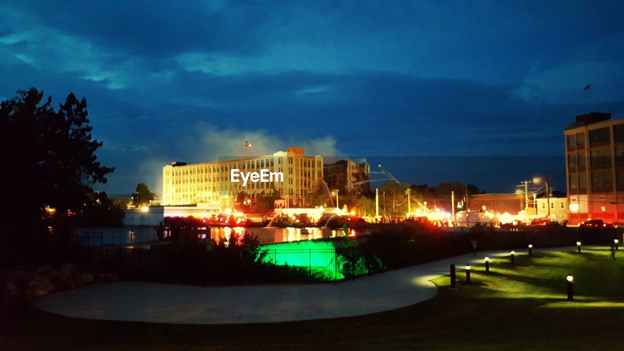 ILLUMINATED CITY BY TREES AGAINST SKY AT NIGHT