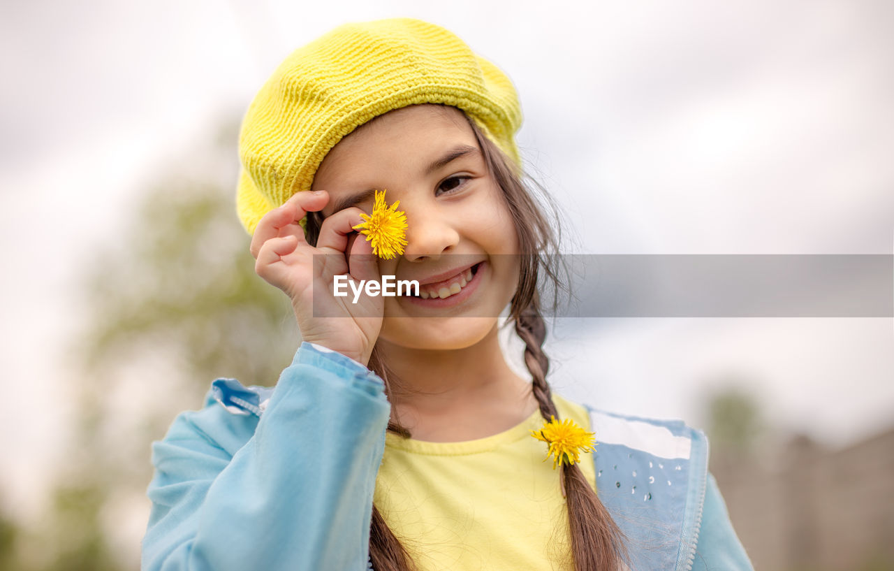 Portrait of a funny charming little girl with two pigtails, in a yellow knitted beret