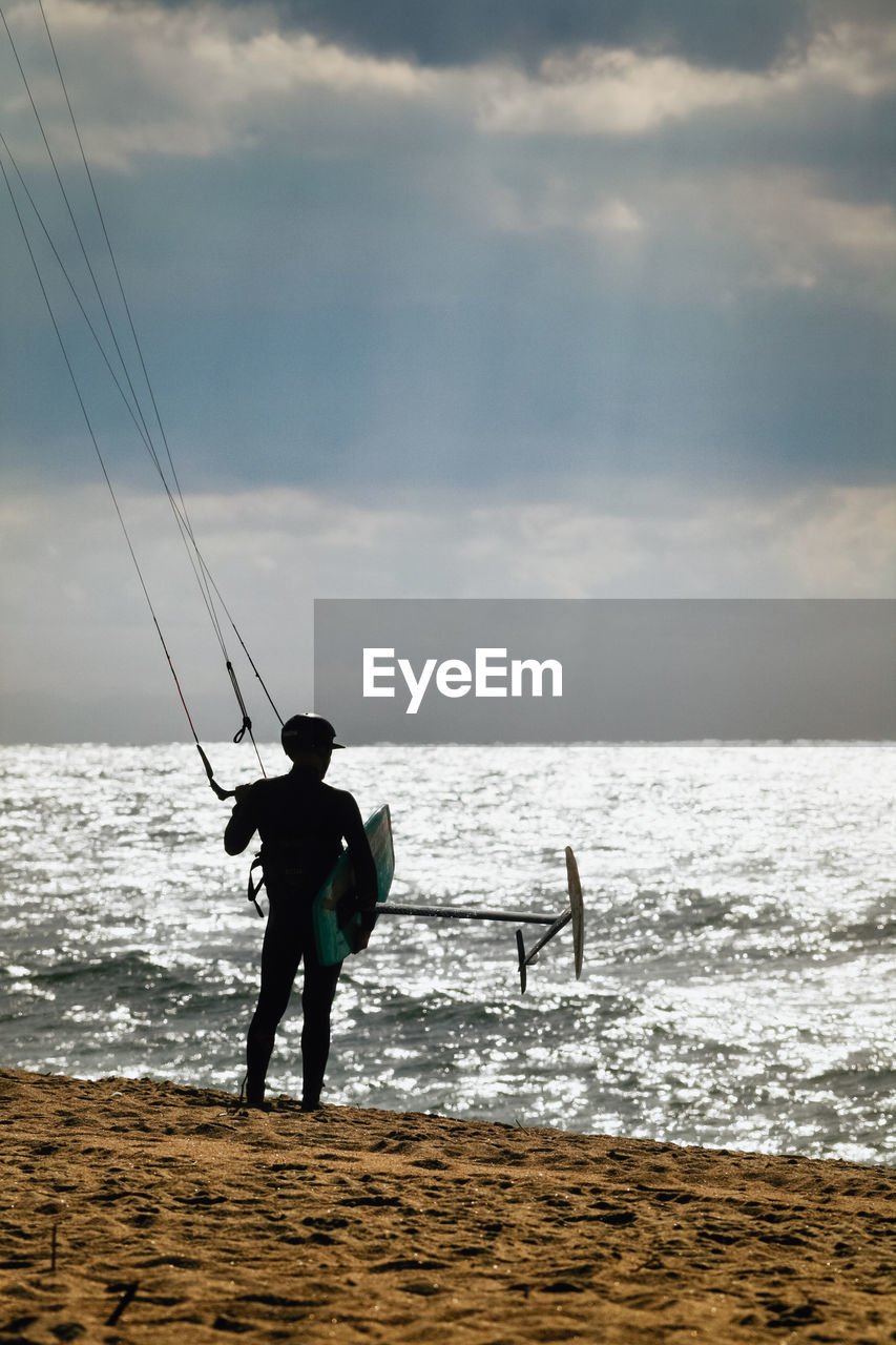 Rear view of windsurfer standing at beach against sky