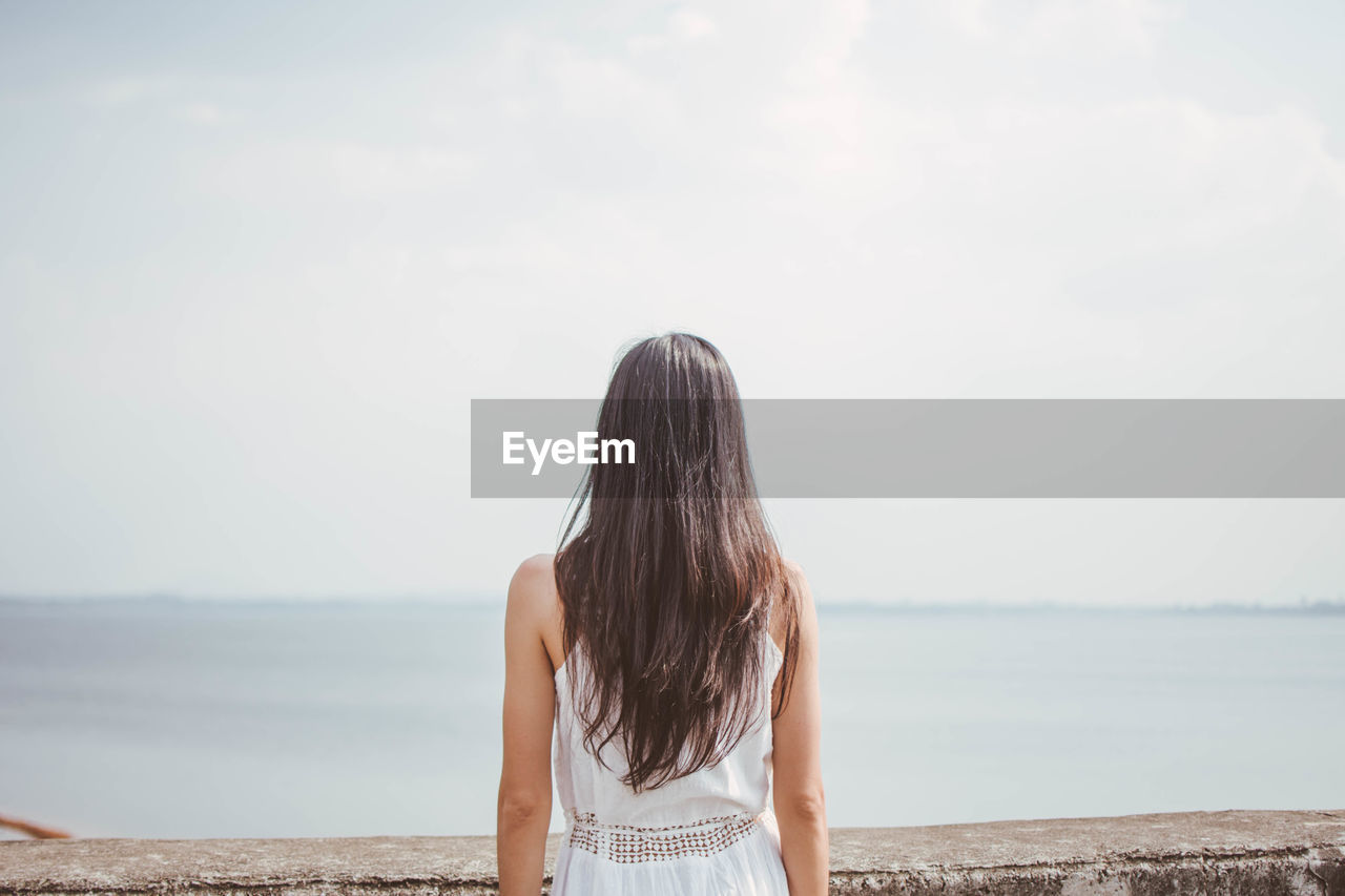 Rear view of woman standing by retaining wall against sky