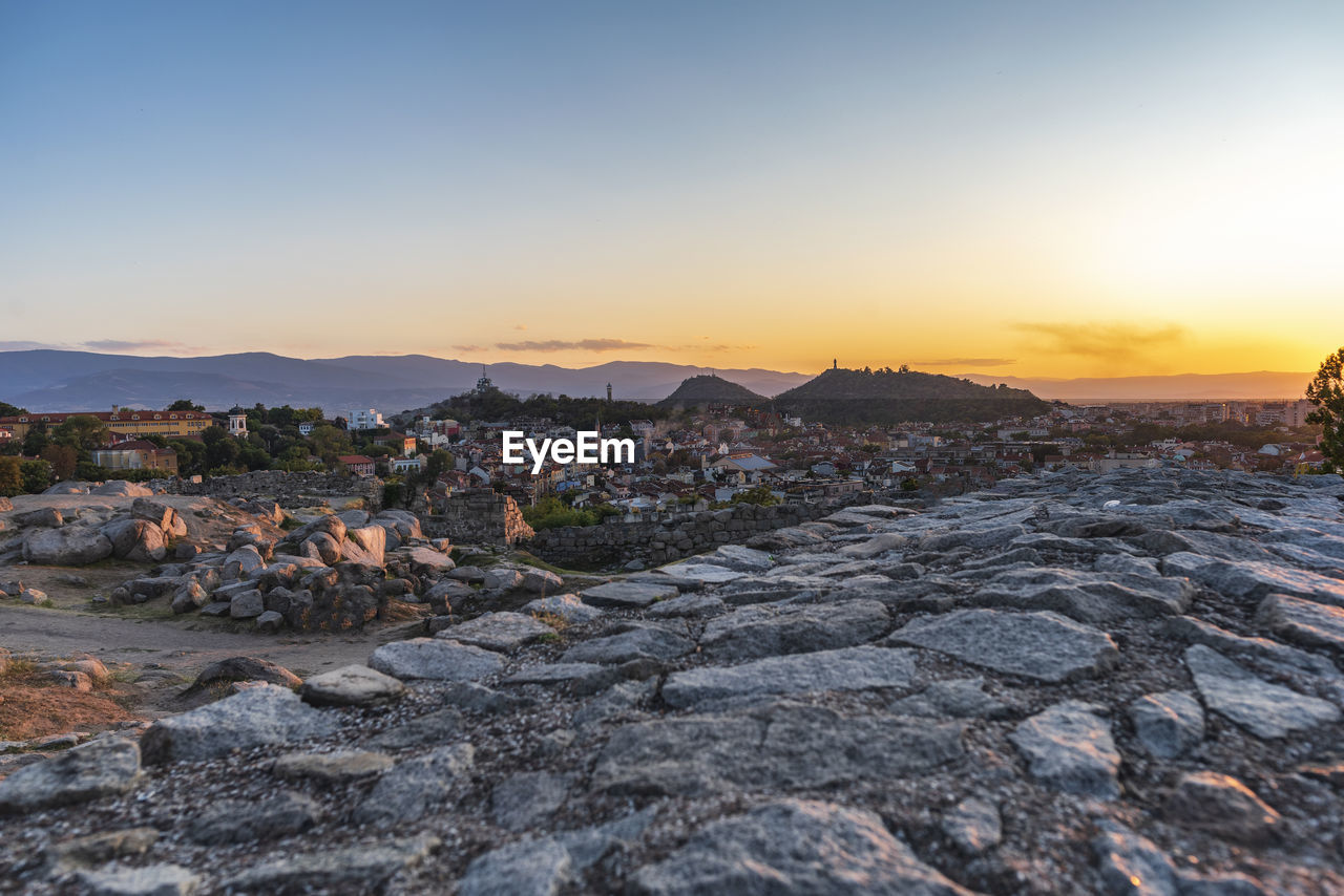 Rocks in city against clear sky during sunset