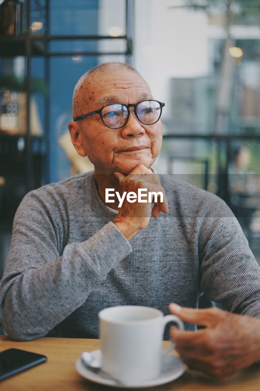 Thoughtful senior man with coffee on table sitting in cafe