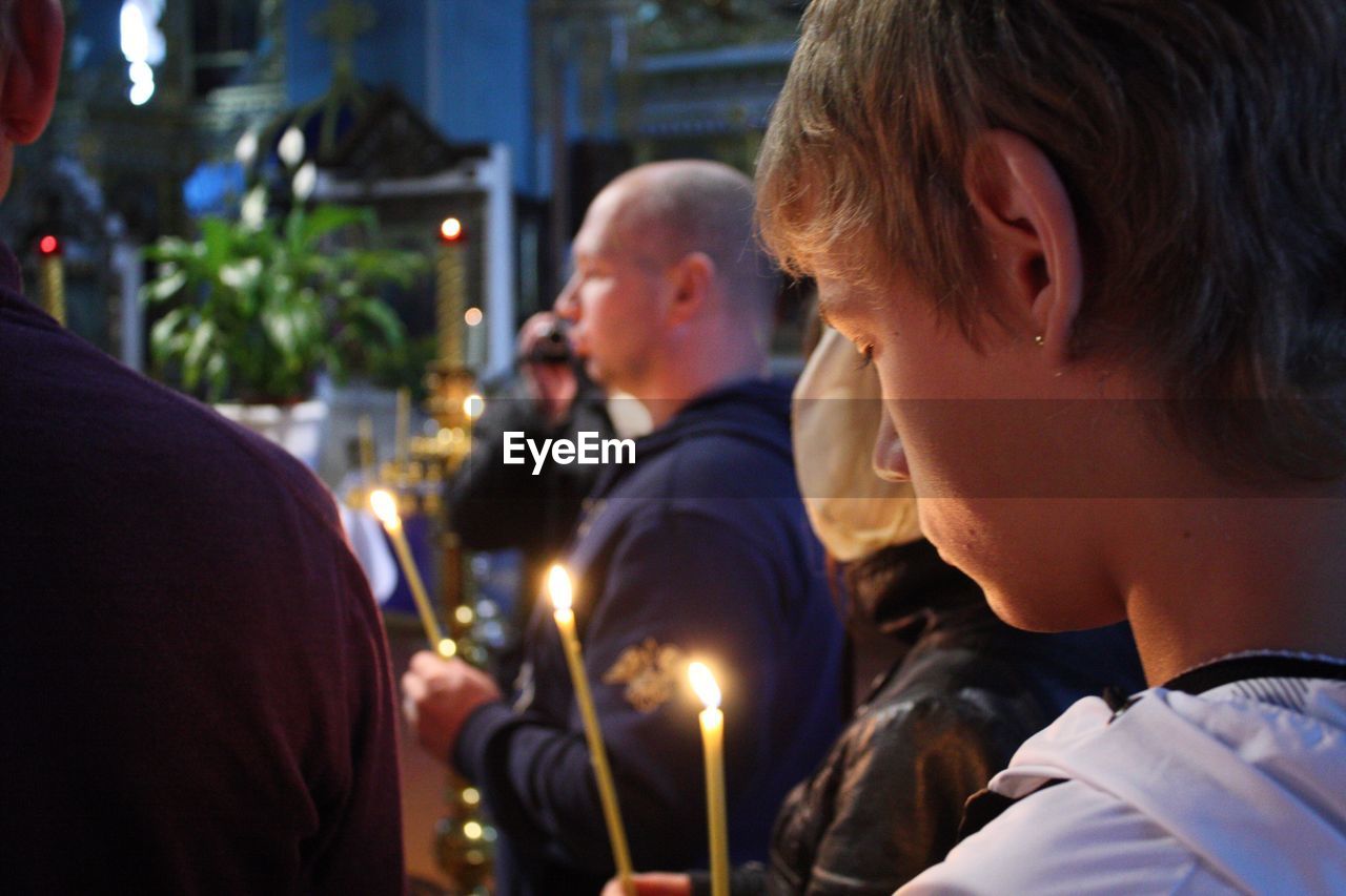 Close-up of woman praying with lit candle in church