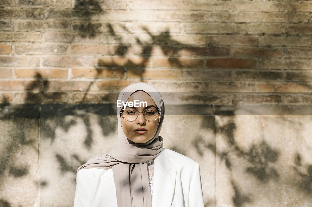 Young woman wearing headscarf while standing in front of wall during sunny day