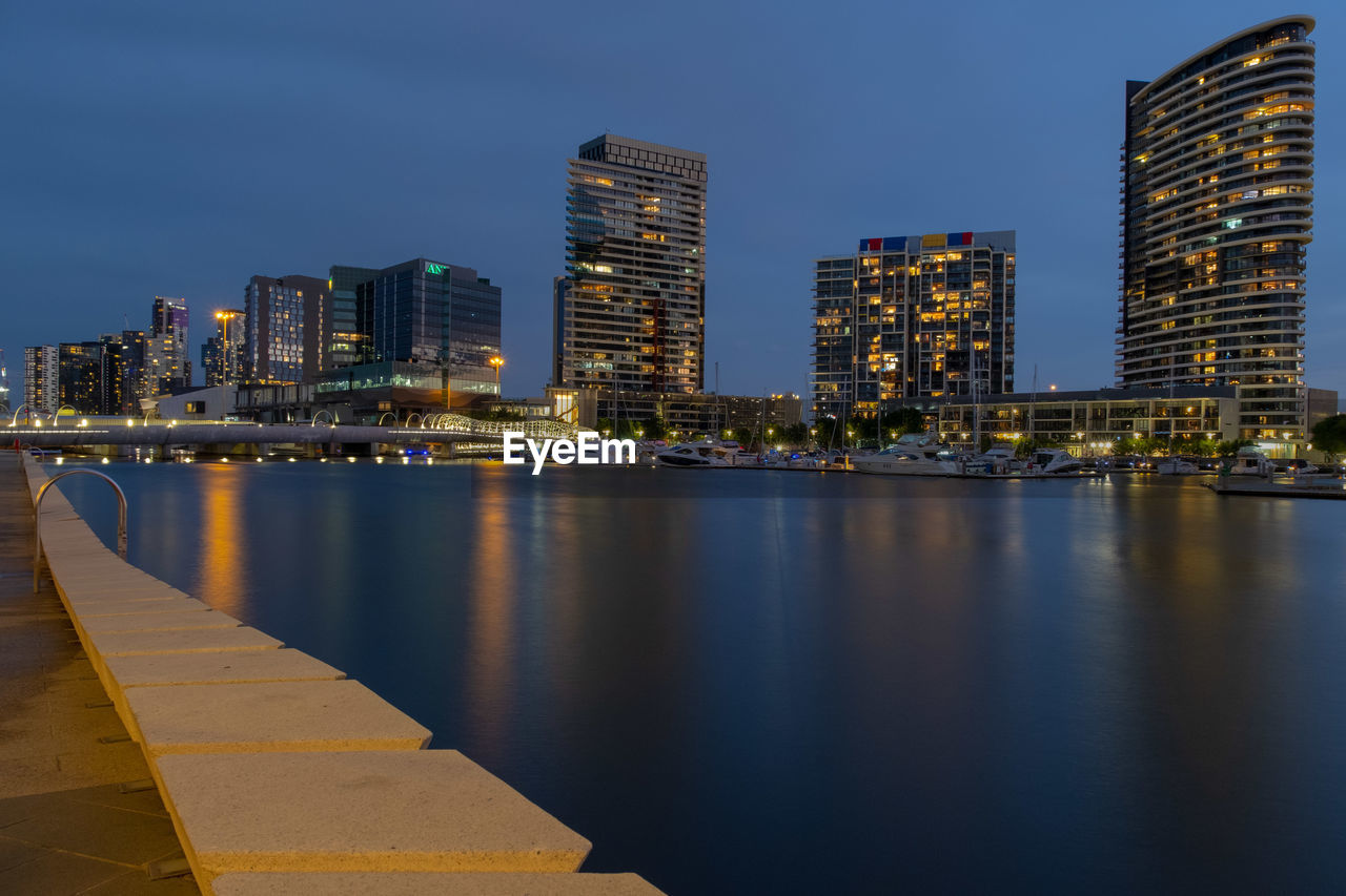 Illuminated buildings by river against sky at night