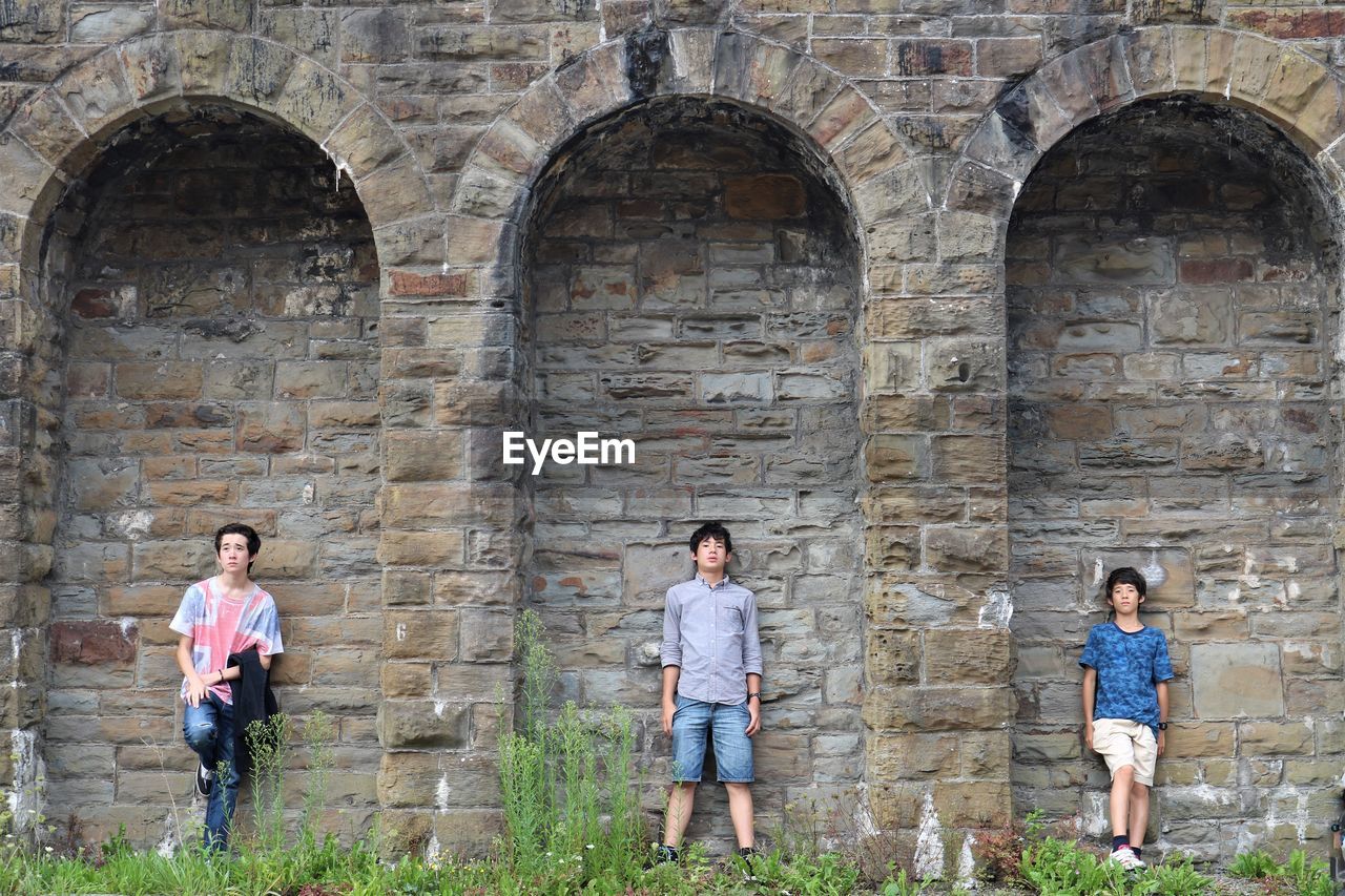 Full length of teenage brothers standing under arches against historic wall