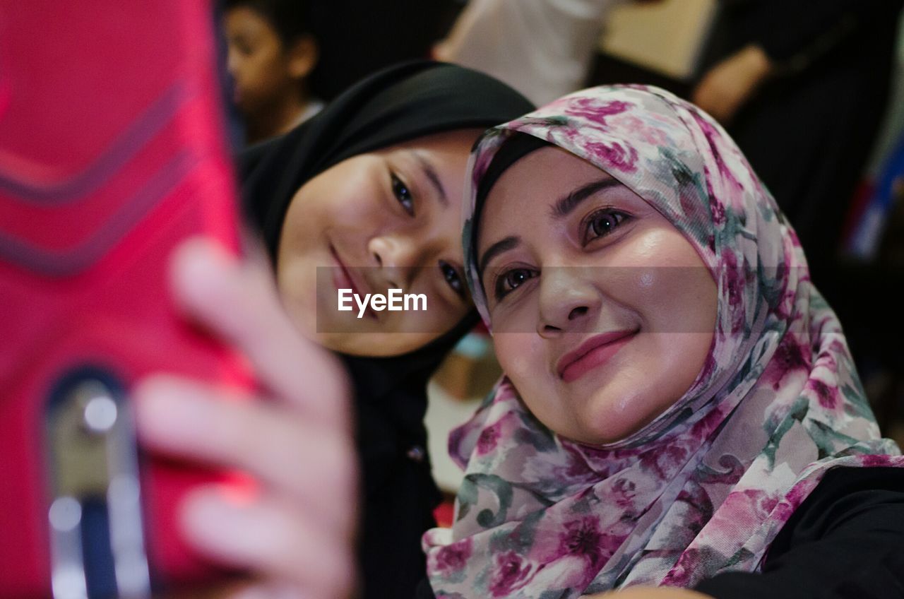 Young woman wearing hijab taking selfie with friend from mobile phone