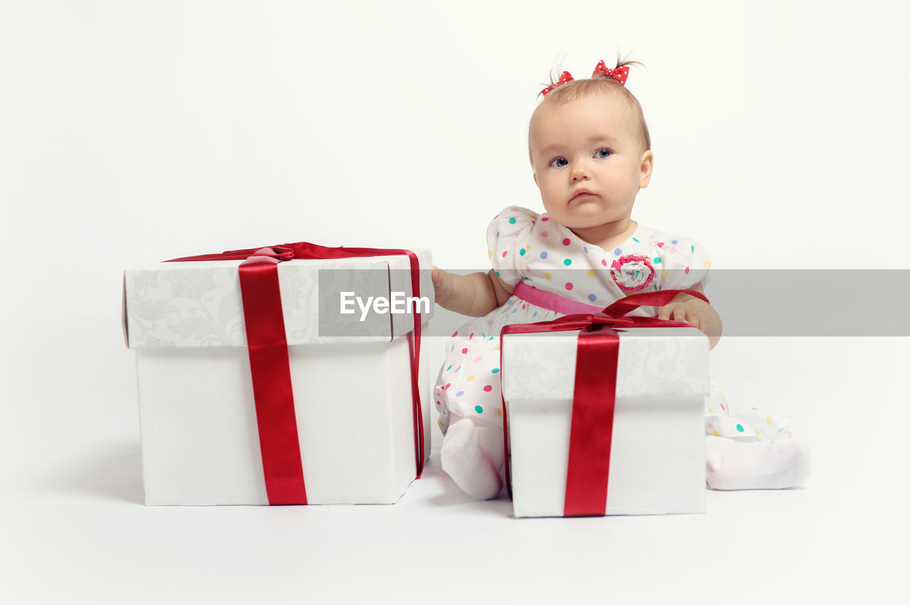 Cute baby girl with christmas gifts sitting against white background