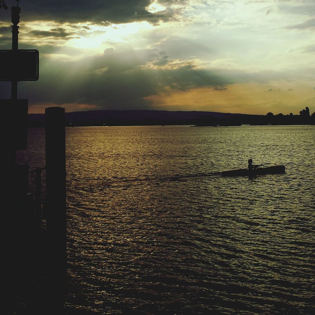 Silhouette person boating on river with cloud sky in background