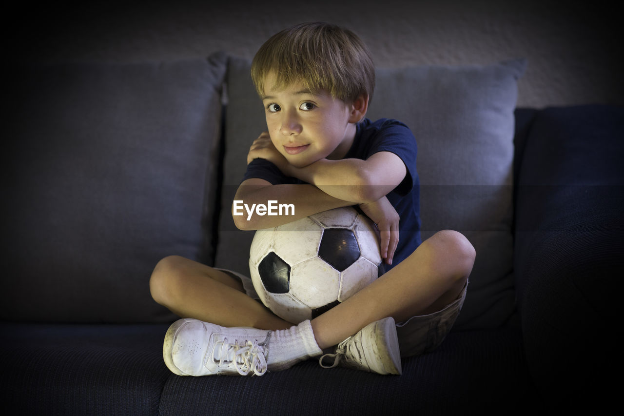 Portrait of boy with soccer ball sitting on sofa at home