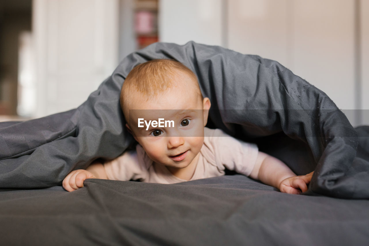 Surprised baby lies on the bed under the blanket