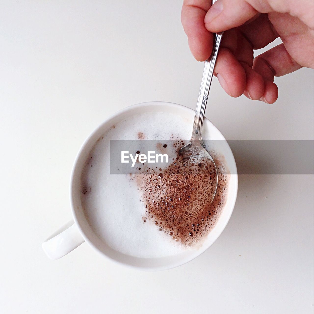 Cropped hand holding spoon in coffee on table