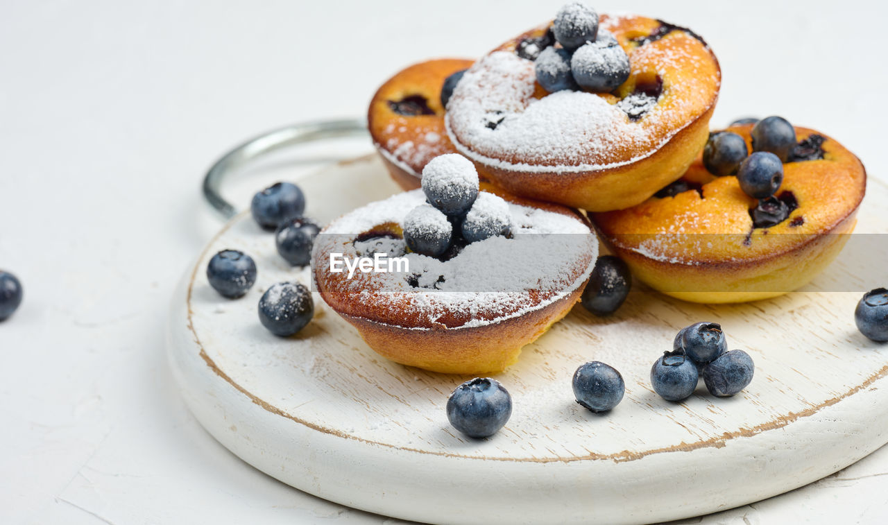 Round mini cottage cheese pies with blueberries on a white wooden board, delicious sweet dessert