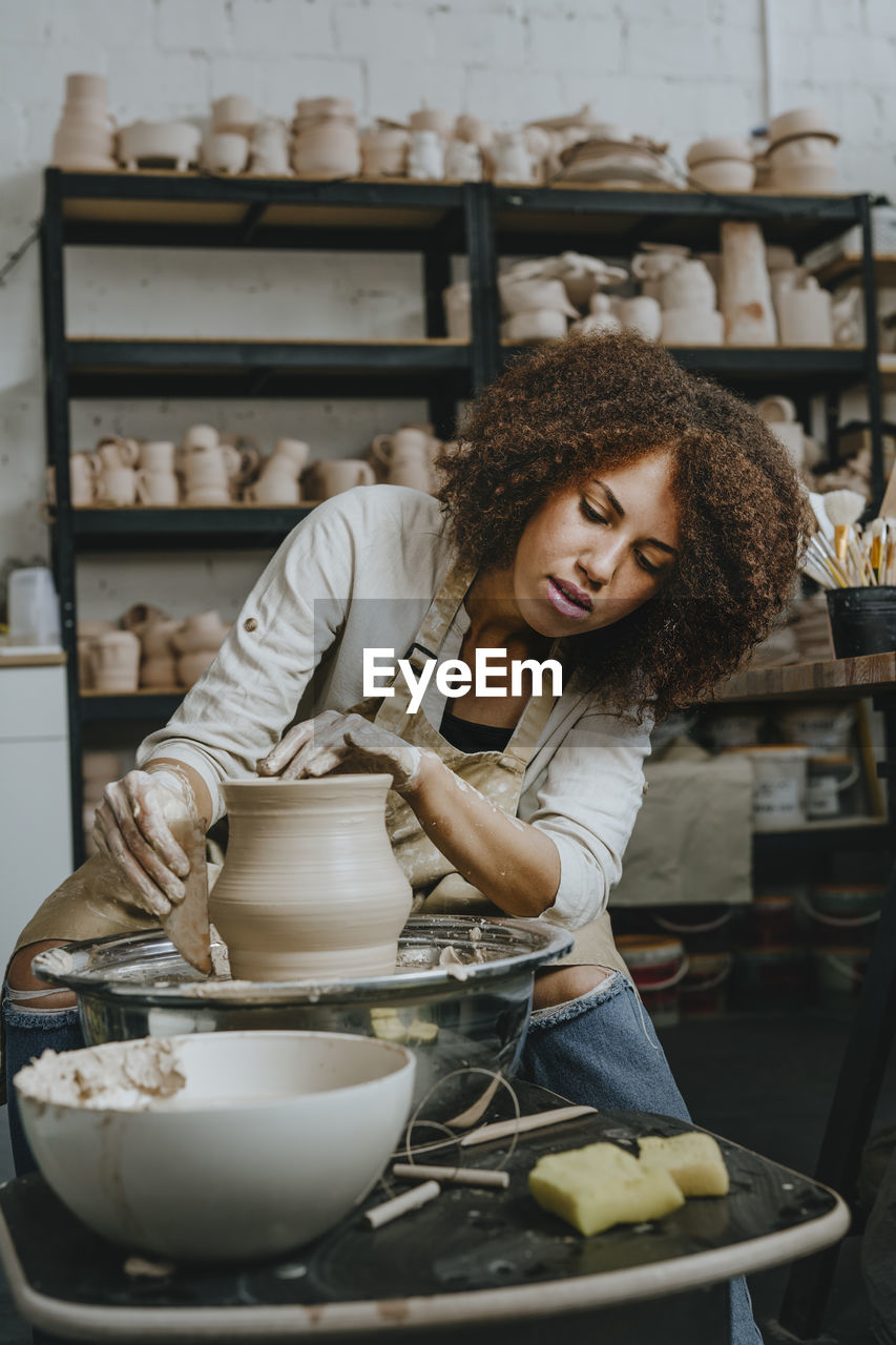 Young craftswoman molding pot shape on pottery wheel