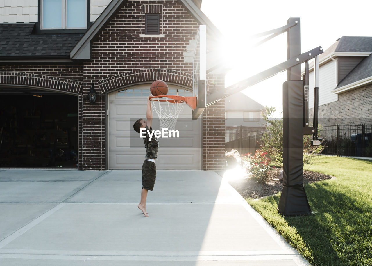 Side view of boy playing basketball in yard