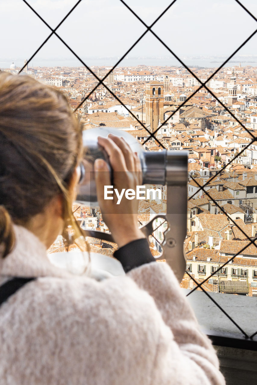 Woman looking city through binoculars