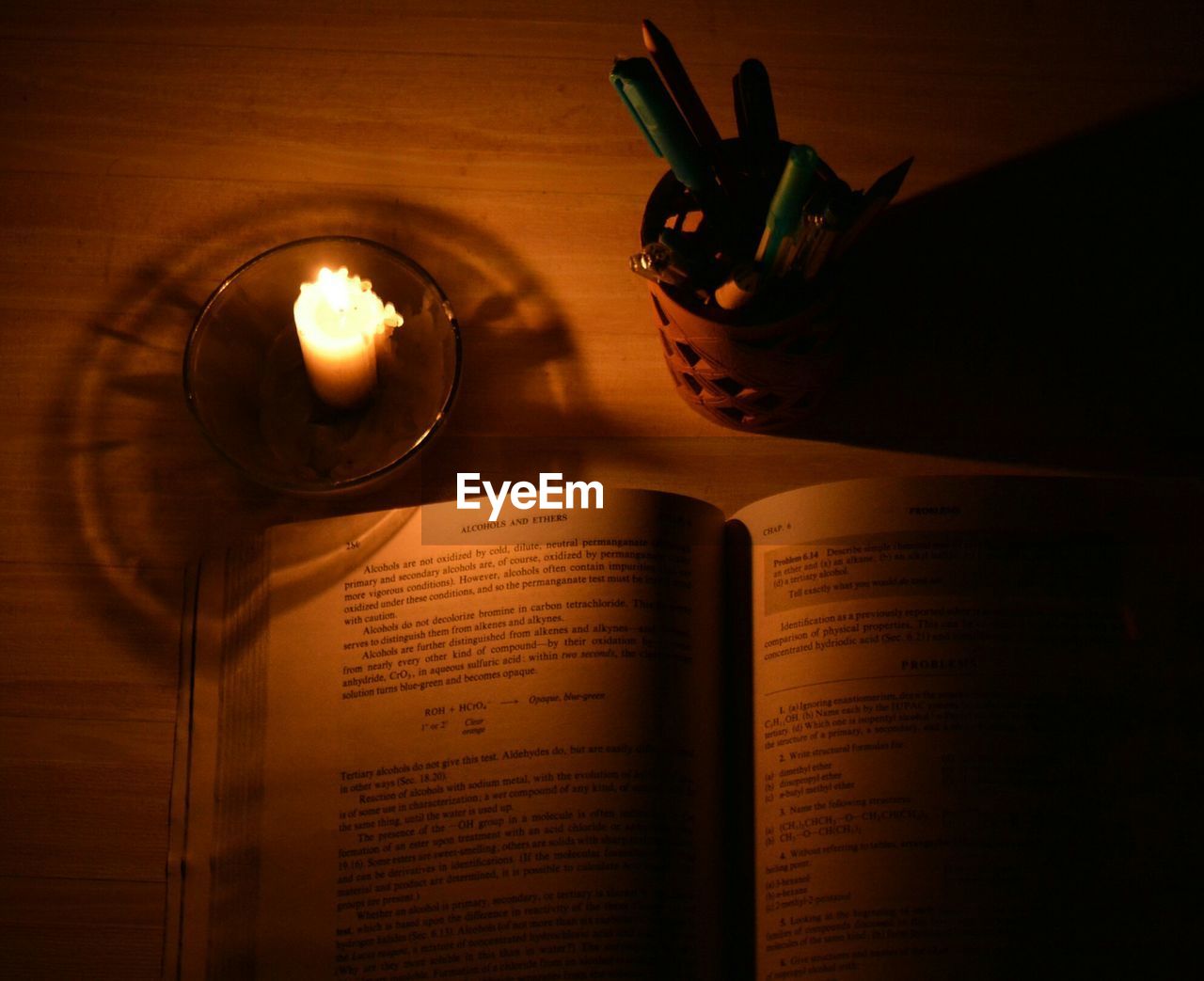 High angle view of book and desk organizer by illuminated candle on table