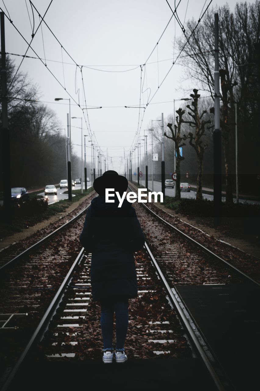 Rear view of woman standing on railroad track against clear sky