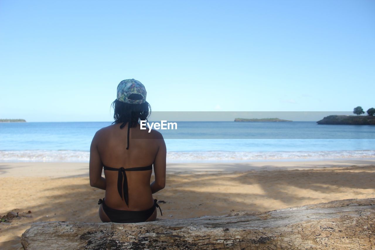 Rear view of woman on beach against clear sky