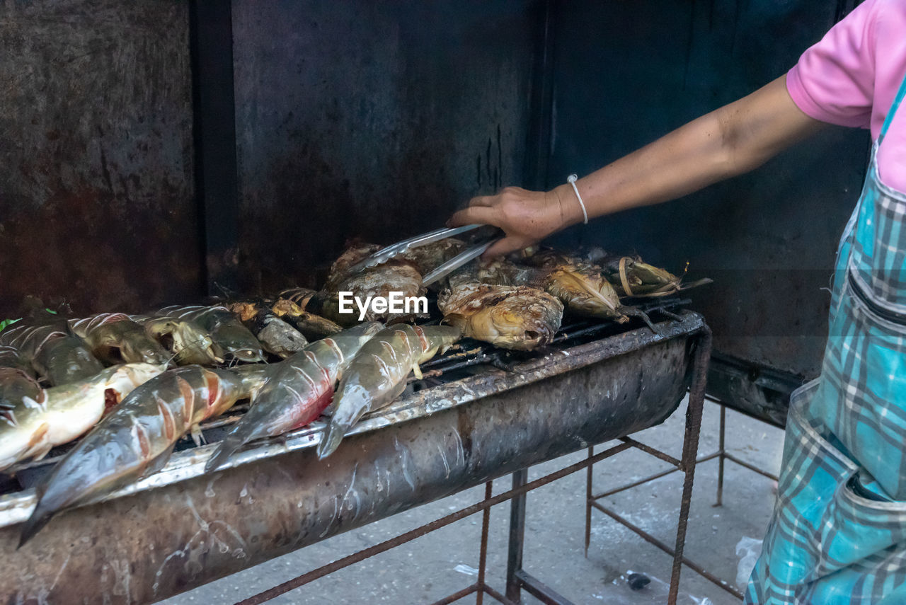 MAN PREPARING FOOD ON BARBECUE GRILL AT MARKET