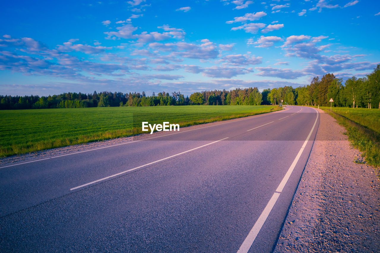 road, sky, landscape, horizon, transportation, environment, nature, plant, land, cloud, scenics - nature, tree, rural scene, highway, beauty in nature, no people, morning, blue, the way forward, travel, asphalt, grass, tranquility, field, non-urban scene, infrastructure, lane, street, tranquil scene, outdoors, country road, diminishing perspective, sunlight, vanishing point, symbol, forest, summer, travel destinations, day, urban skyline, green, road marking, road surface, idyllic