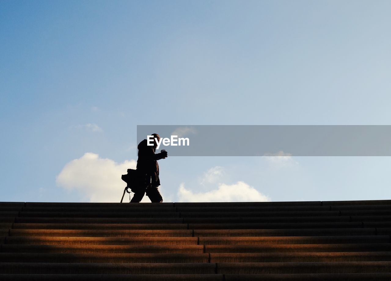 FULL LENGTH OF MAN STANDING ON STAIRCASE AGAINST SKY