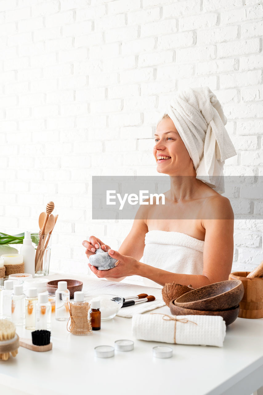 Young woman wearing white bathrobes towels on head doing spa procedures mixing natural ingredients