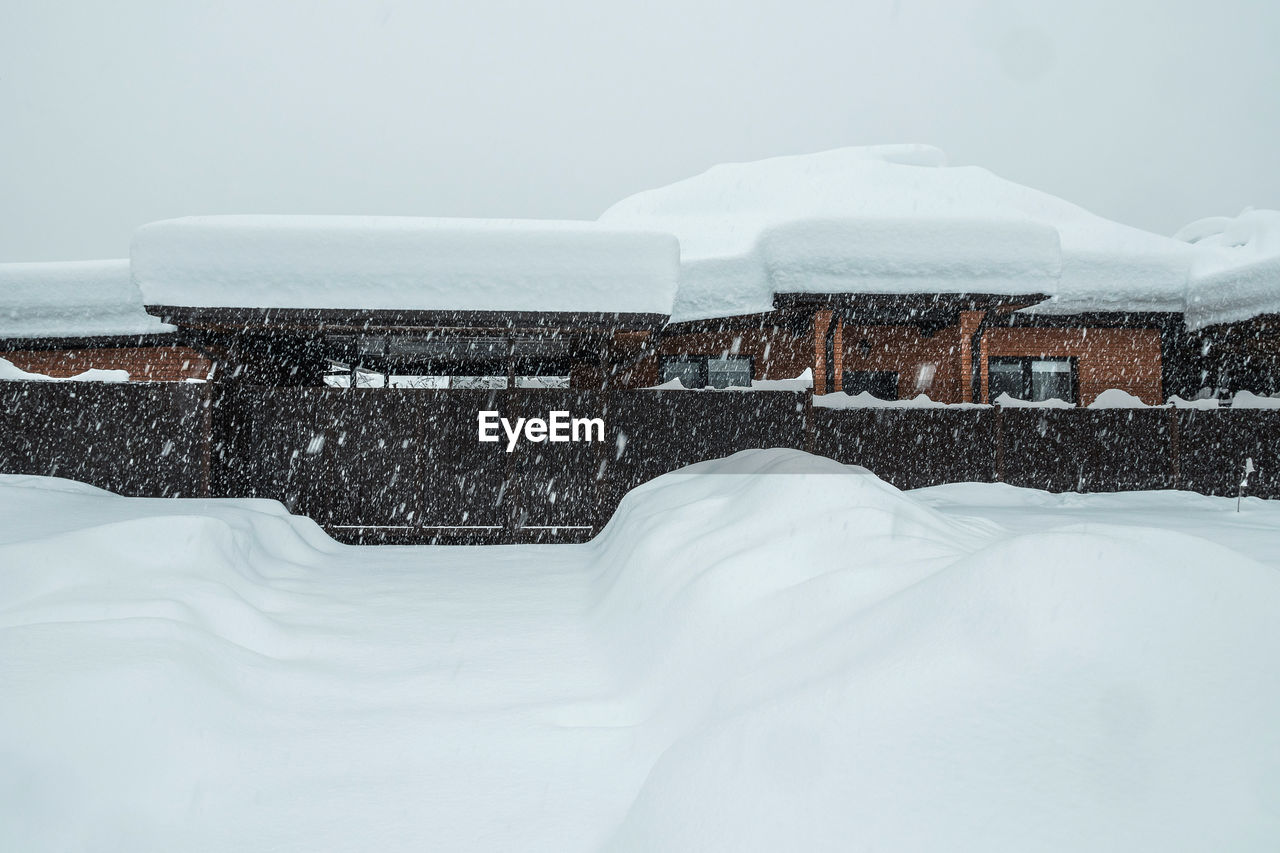 A brick house and street covered with snow. there is a thick layer of snow on roof of the house