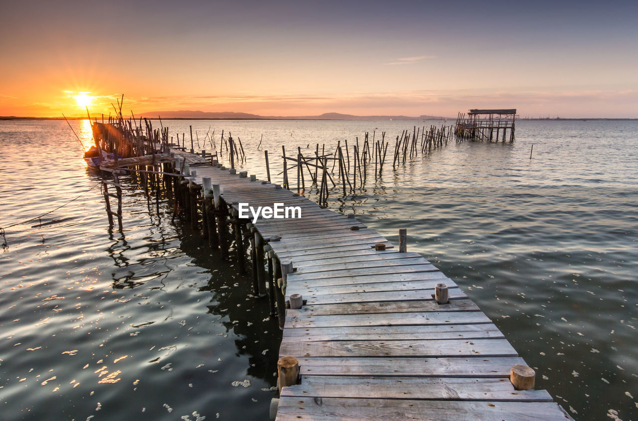 Wooden pier over sea against sky during sunset