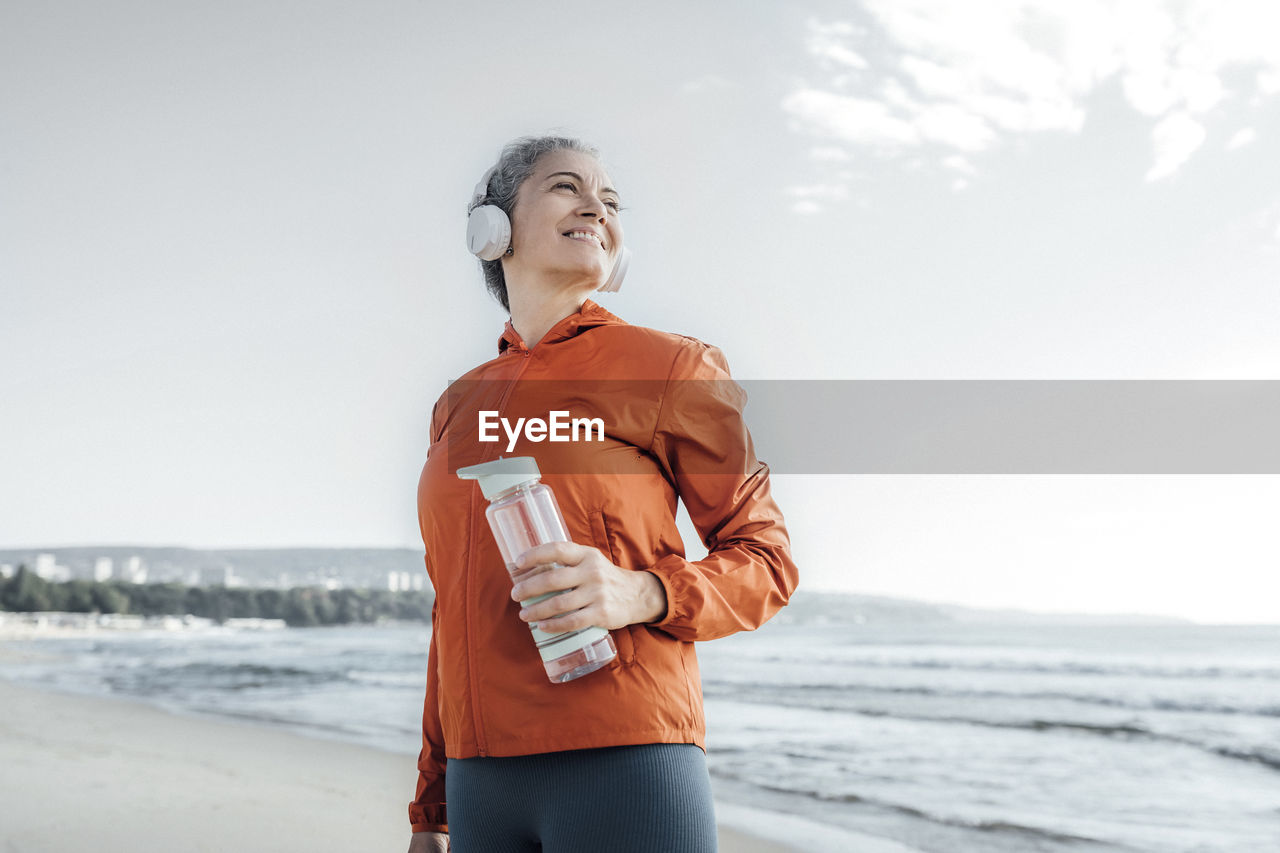 Smiling mature woman with water bottle on beach